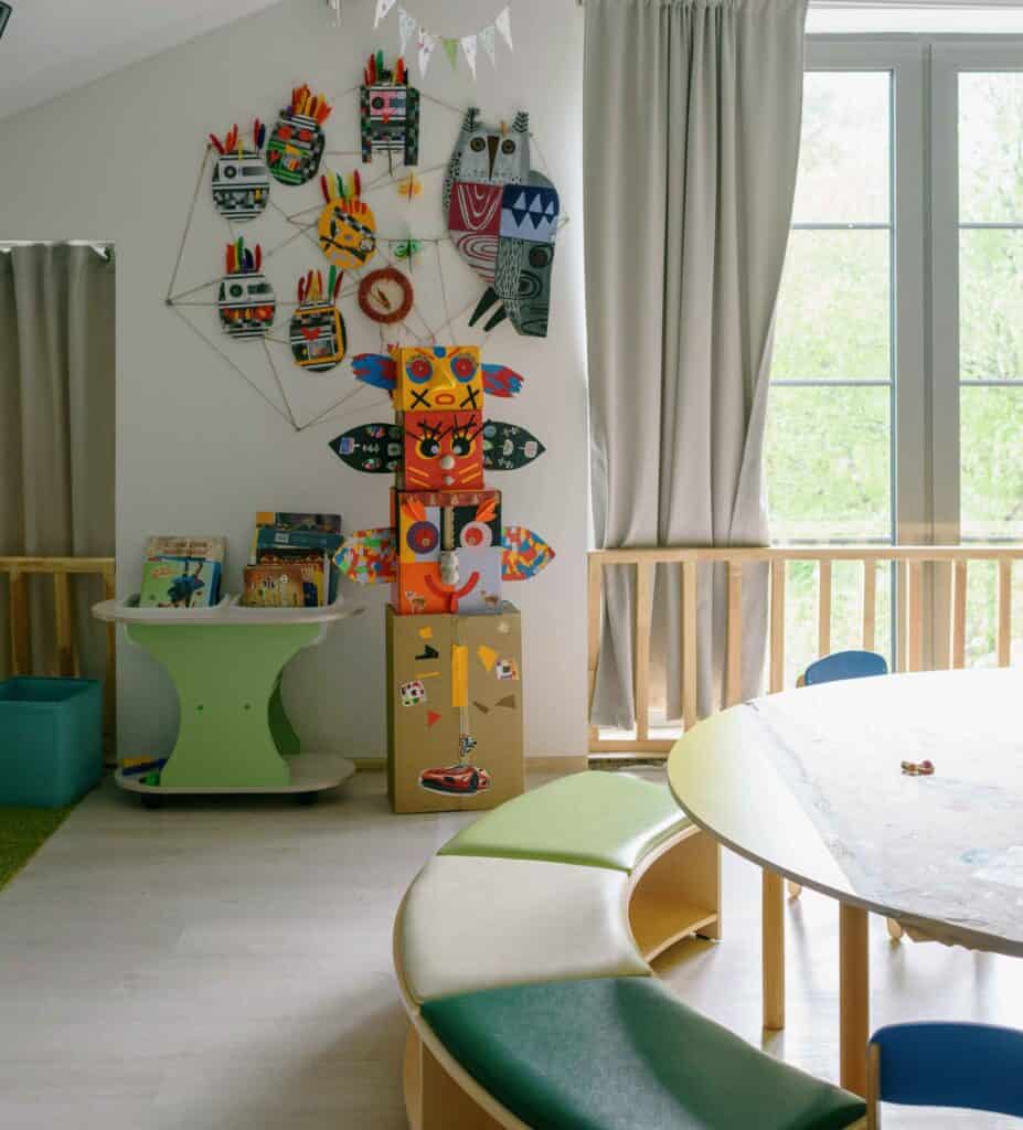 child's nursery with green themed table and chairs and light green curtains and owl pictures on the wall